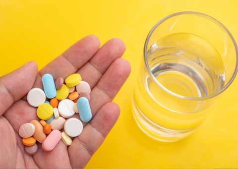 hand holding a variety of colorful pills, with a glass of water next to it.
