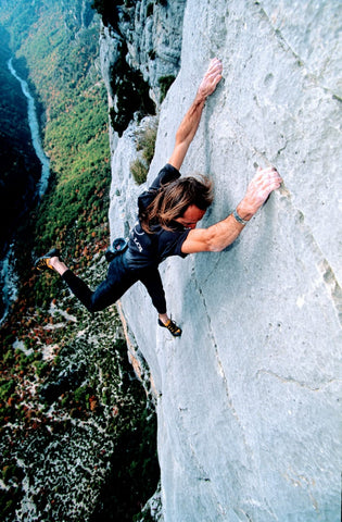 Alain Robert hanging by his hands from a sheer cliff face