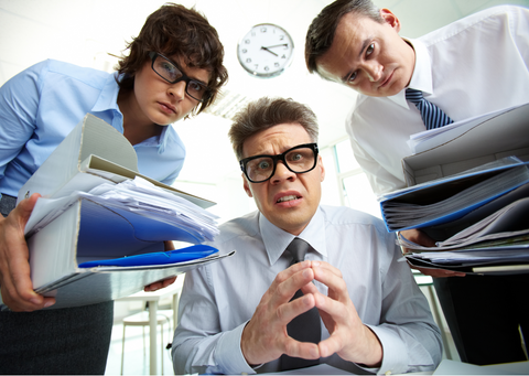 a white woman and 2 white mean in business attire leaning over and staring at the camera with lots of folders in their hands.