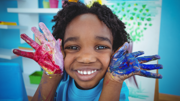 Happy black kid's face with their hands covered in paint next to their face