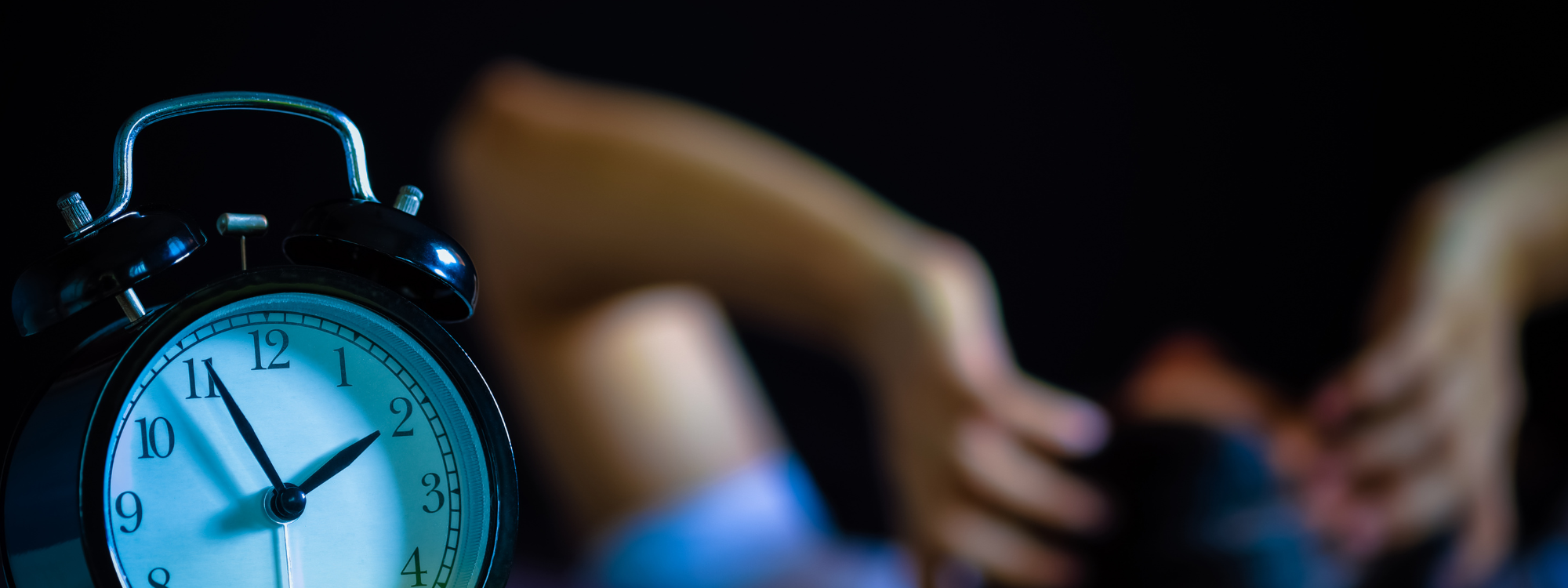 Close up of an alarm clock, with a blurry awake human in the background