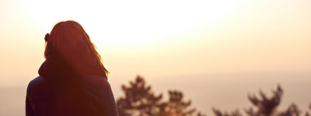 Woman from the back looking across hills to the sunset