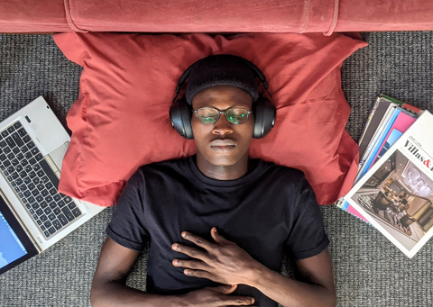 Young black man lying down with his eyes closed, wearing headphones and looking peaceful