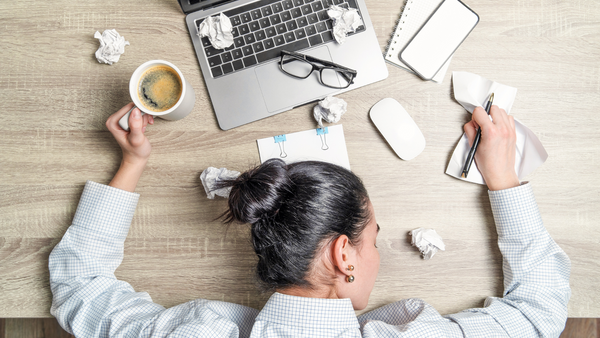 woman with head on desk and work stuff scattered around her