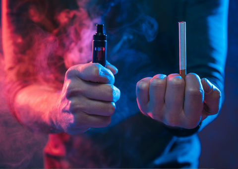 man holding a vape pen in one fist and a cigarette in the other