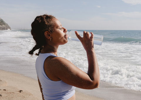 woman drinking bottle of water on a beach