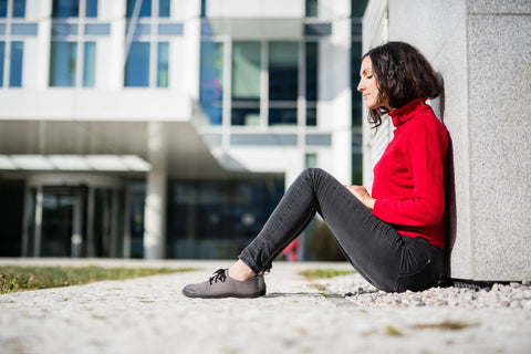 Eine Frau in Ahinsa-Barfußschuhen sitzt auf dem Boden und lehnt sich an eine Wand