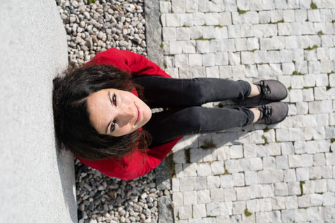 A smiling woman sitting on the ground in barefoot shoes.