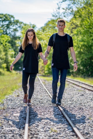 A man and woman in barefoot shoes walking along train tracks holding hands. 