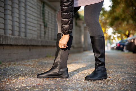 Eine Frau, die barfuß kniehohe Ahinsa-Stiefel mit einem Reißverschluss an der Seite befestigt