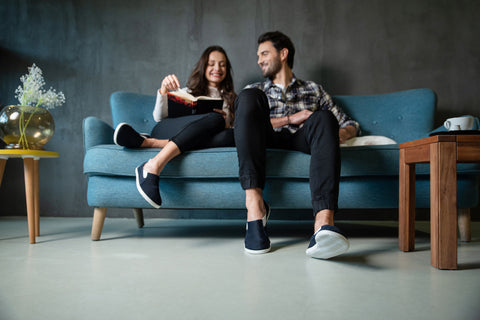 Woman and man sitting on a couch, both wearing barefoot slip-on sneakers