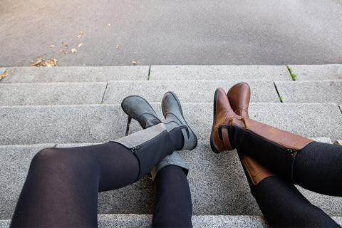 Two women sitting next to each other, one wearing grey barefoot Ahinsa boots and the other wearing brown ones
