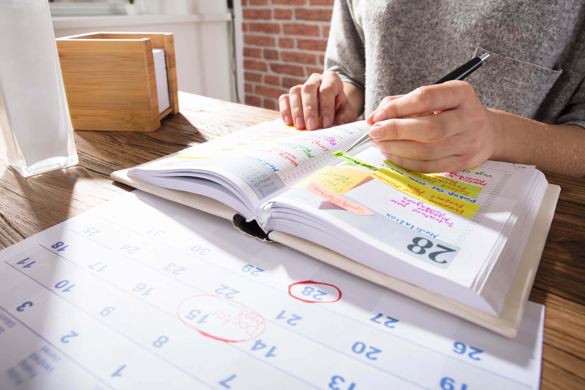 a left-handed woman preparing her schedule on her notepad, at her beautiful wooden table.