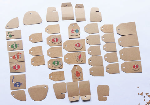 Forty three cardboard gift tags cut from an EcoSplat reusable water balloon box. They are small and different shapes and have holes punched in the tops