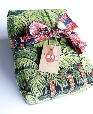 A present gift wrapped in fabric, tied with a ribbon, with a gift tag showing an EcoSplat Reusable Water balloon red cartoon character.