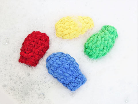 Four EcoSplat reusable water balloons (red, blue, green, yellow) floating in a bubble bath