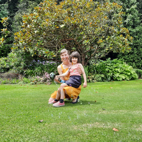 Anthea Madill in a sunny garden with her daughter sitting on her knee. They are smiling at the camera.