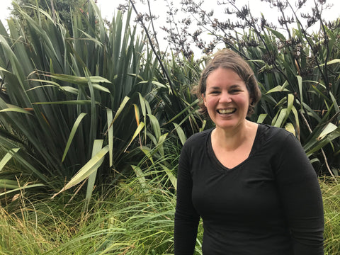 Helen Townsend standing in front of flax bushes smiling at the camera