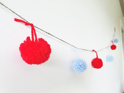 Red and blue pompoms hanging on a string against a white wall