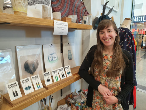 Anthea Madill standing in a shop in front of a display of Remix Plastic earrings and smiling at the camera.