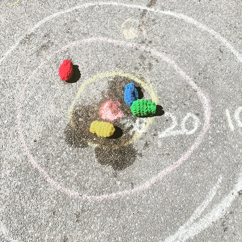 Concentric circles drawn on concrete with chalk. Four EcoSplat reusable water balloons are on the target with water splashes. 