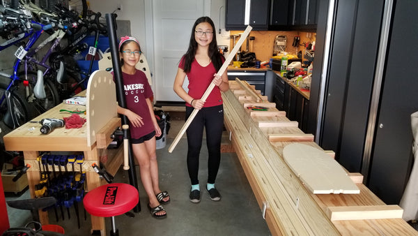 Two young canoebuilders stand beside their materials in a woodshop