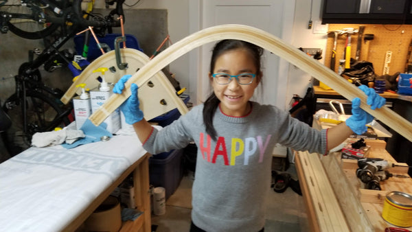 A young canoe builder poses with the wood bent stems of a canoe