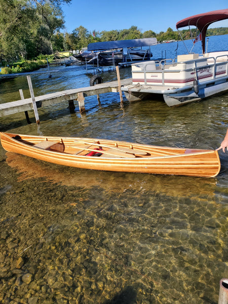 A completed Bob's Special wooden canoe floats in shallow water
