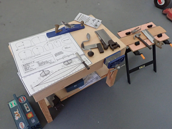 A scale model workbench with mock canoe plans and hand tools on it