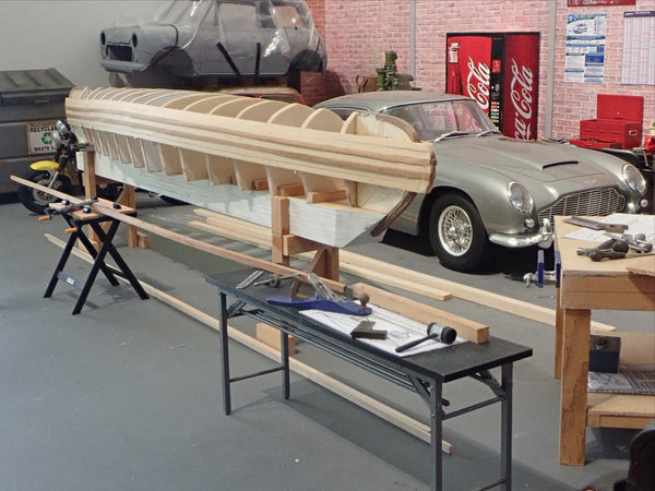 A partially planked scale model canoe beside a scale model vintage car