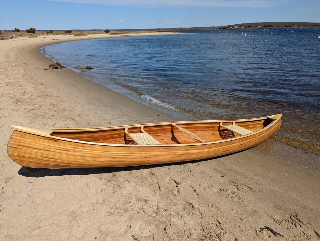 A woodstrip canoe sits on a sandy beach