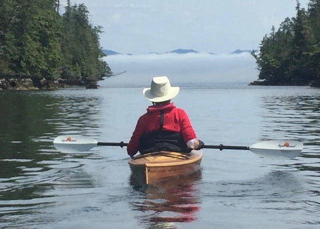 A kayaker sits in a wooden kayak watching mist drift across a bay