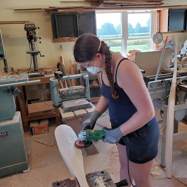 A young woman sands the blade of a canoe paddle