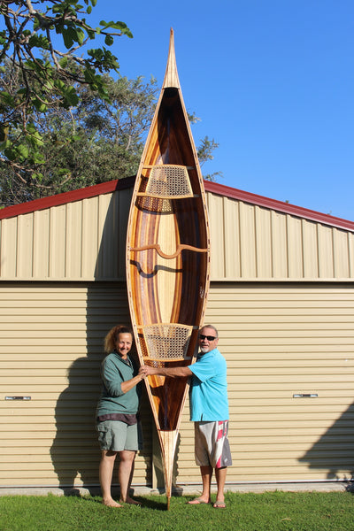 Keith and Nicki stand with finished Champlain canoe upright against a garage