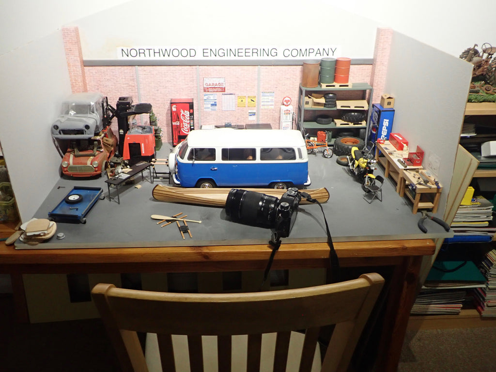 A scale model VW bus and wooden canoe sit on a desk with a camera positioned nearby