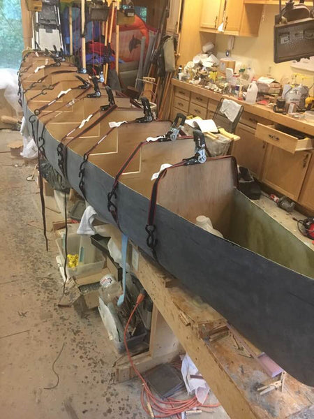 Composite canoe under construction seen with molds inside and tension straps to hold ribs in place while epoxy sets