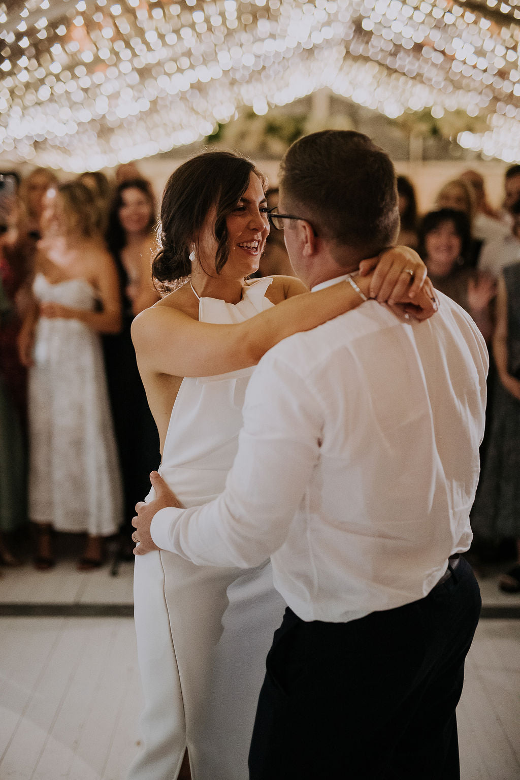 Bride wearing modern white crepe wedding dress dancing with groom inside wedding marquee