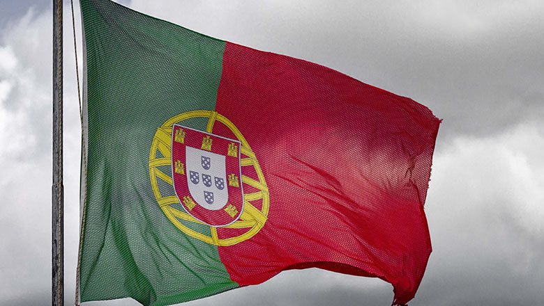 Portugiesische Flagge mit dem Wappen von Portugal weht vor grauen Wolken im Wind.