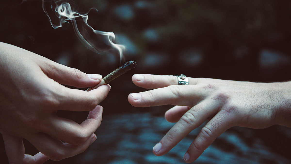 Zwei Hände übergeben sich einen rauchenden Joint mit einem Raw Filter Tip.