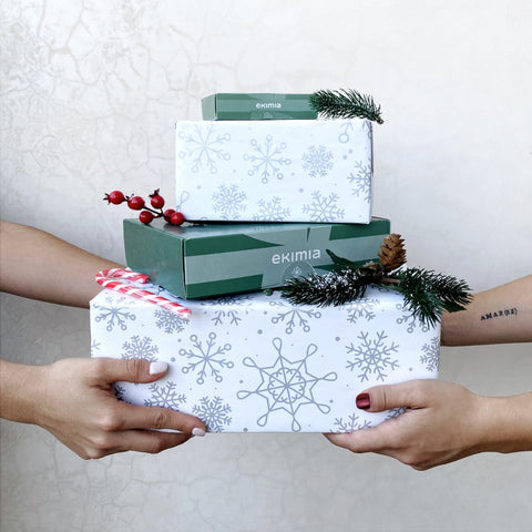 Intercambio festivo: Dos personas comparten alegría navideña, manos extendidas sosteniendo y pasando cajas de regalo bellamente decoradas en un ambiente cálido de celebración.