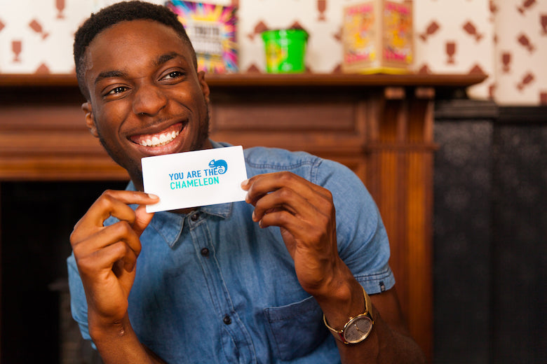 A person showing the others, they are holding the “you are the chameleon” card.