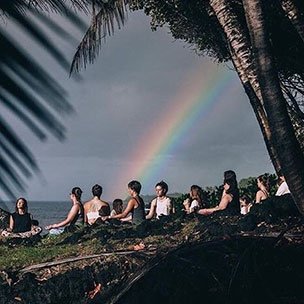 Group meditating outside under a rainbow