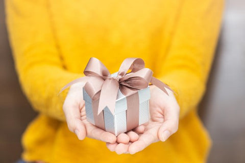 a woman in a yellow jumper holding out a meaningful gift with a ribbon around it.