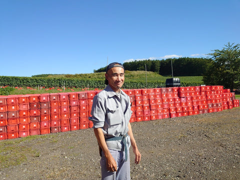 大量の赤いコンテナの前に立つ弘津雄一さんの写真
