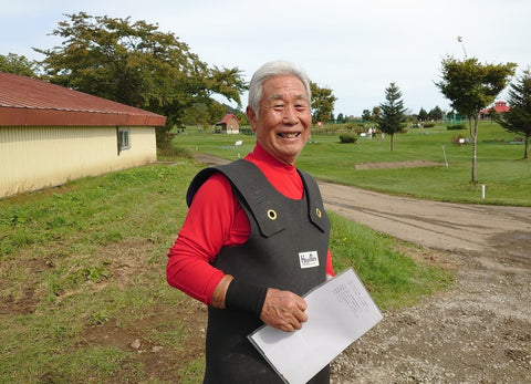 芝生の敷かれた孵化場を背景に笑顔で立つ久保田さんの写真