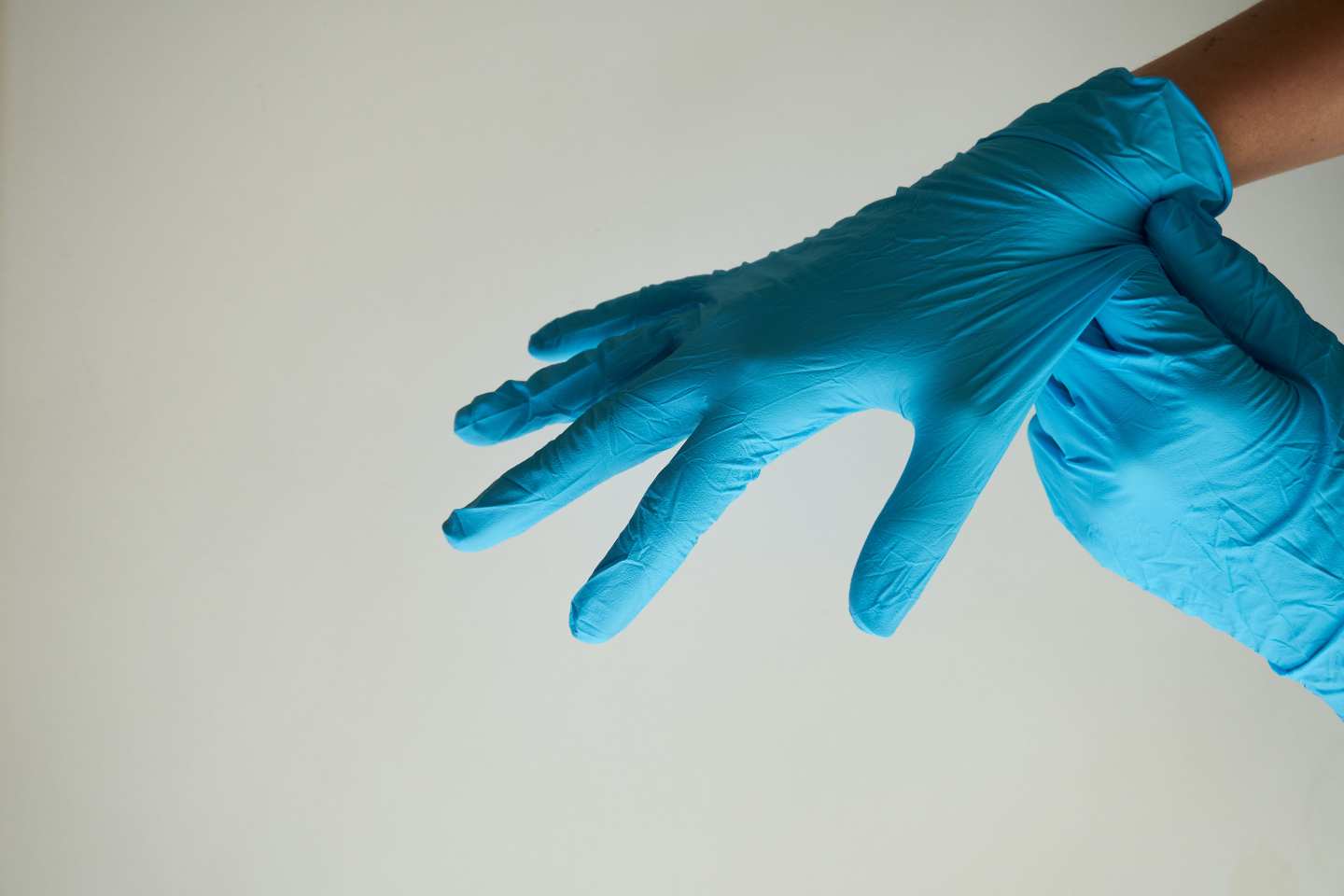 Two hands with blue gloves, one hand pulls the glove onto the other.