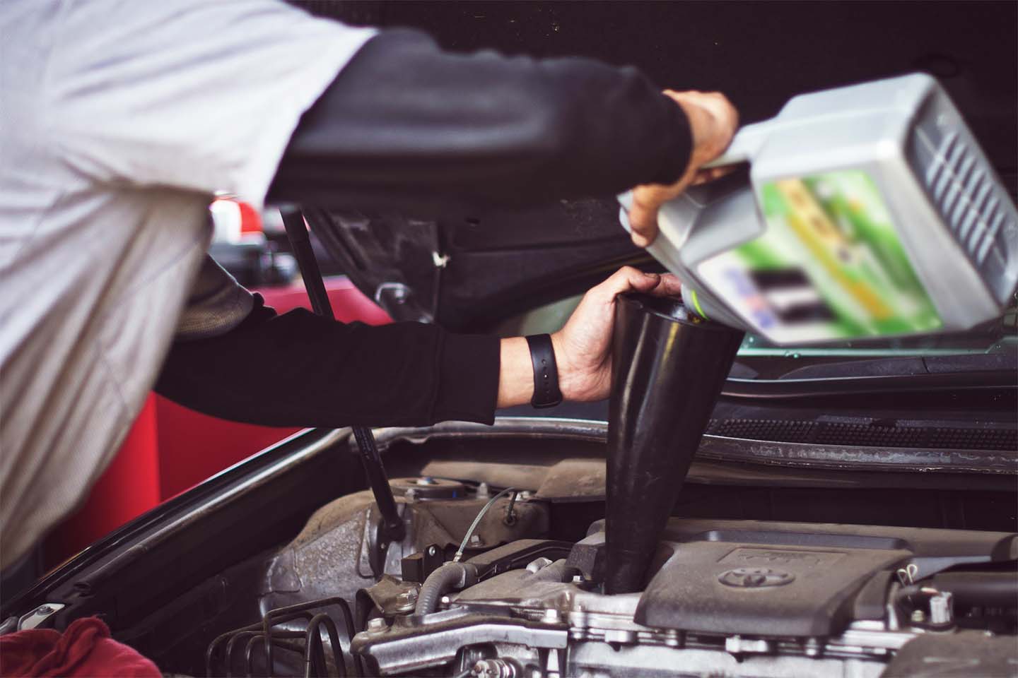 person performs an oil change in car engine, person pours oil into funnel