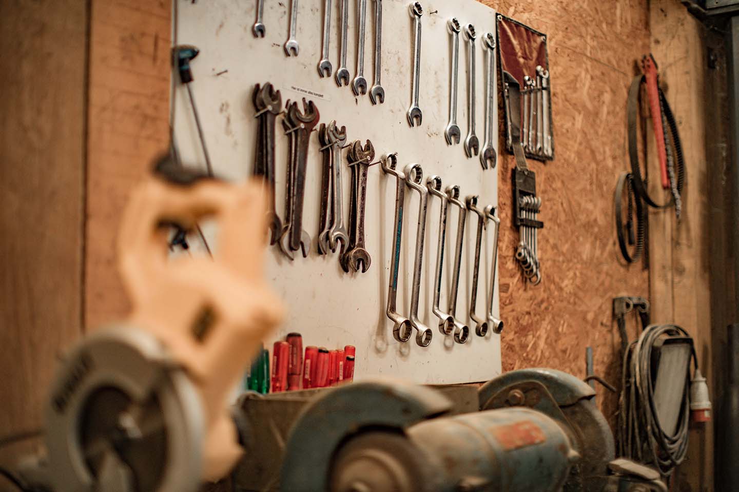 spanners and other mechanic tools hanging on a wall in a workshop
