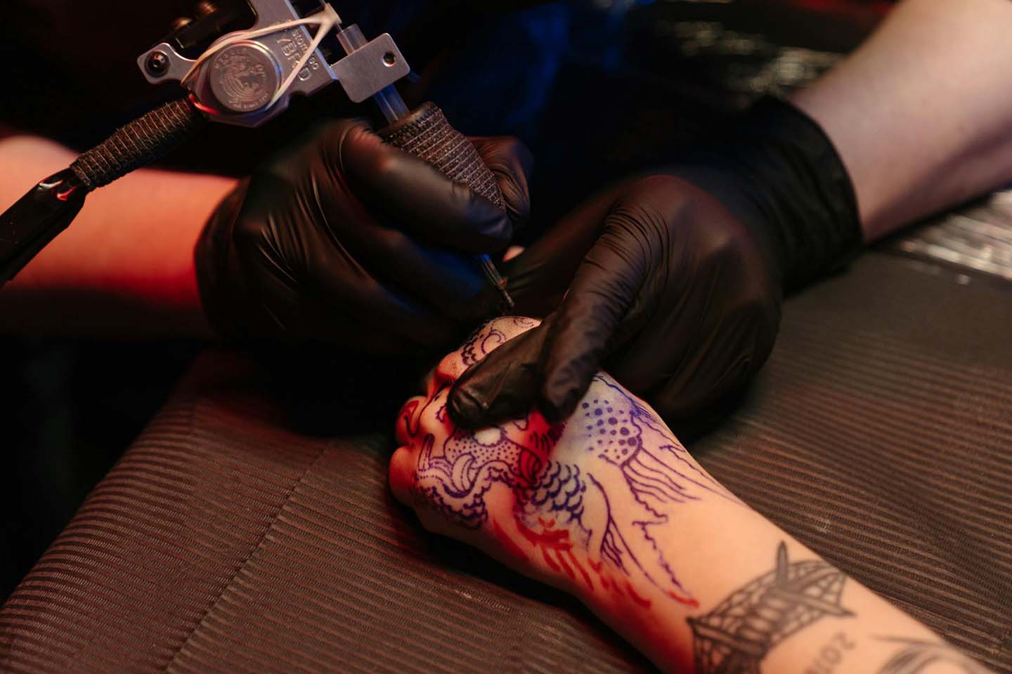 Person giving another person a hand tattoo, wearing black gloves