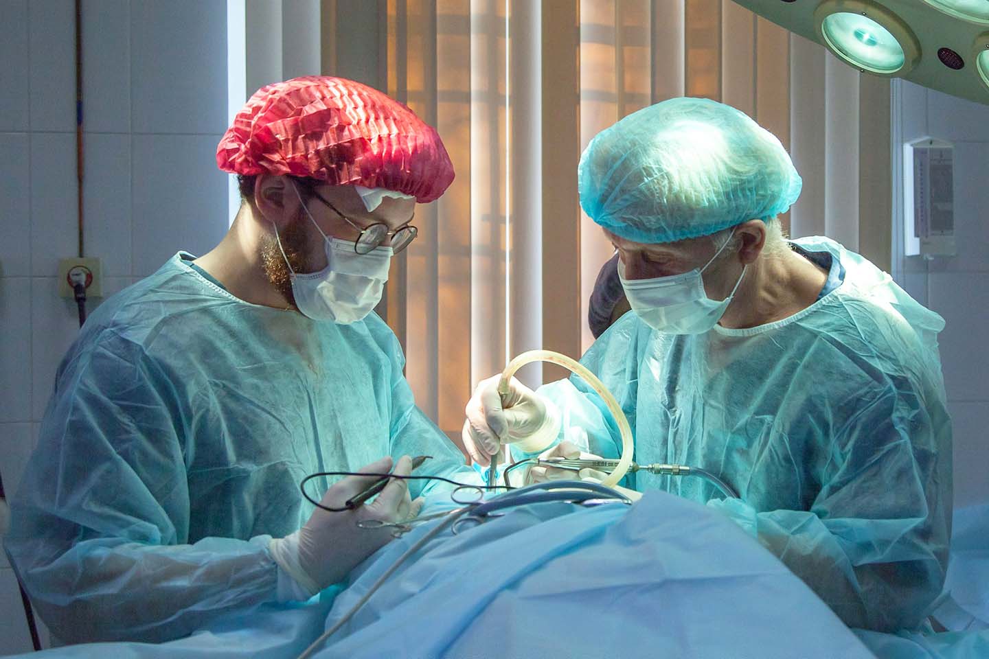 Two surgeons wearing sterile gowns and gloves and doing a surgical operation.